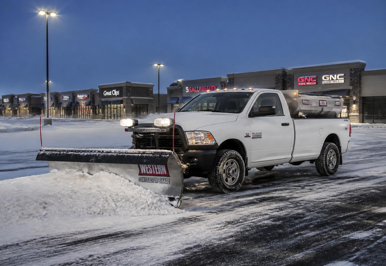Ram 3500 pickup with commercial snow plow and salt spreader clearing a lit commercial plaza parking lot